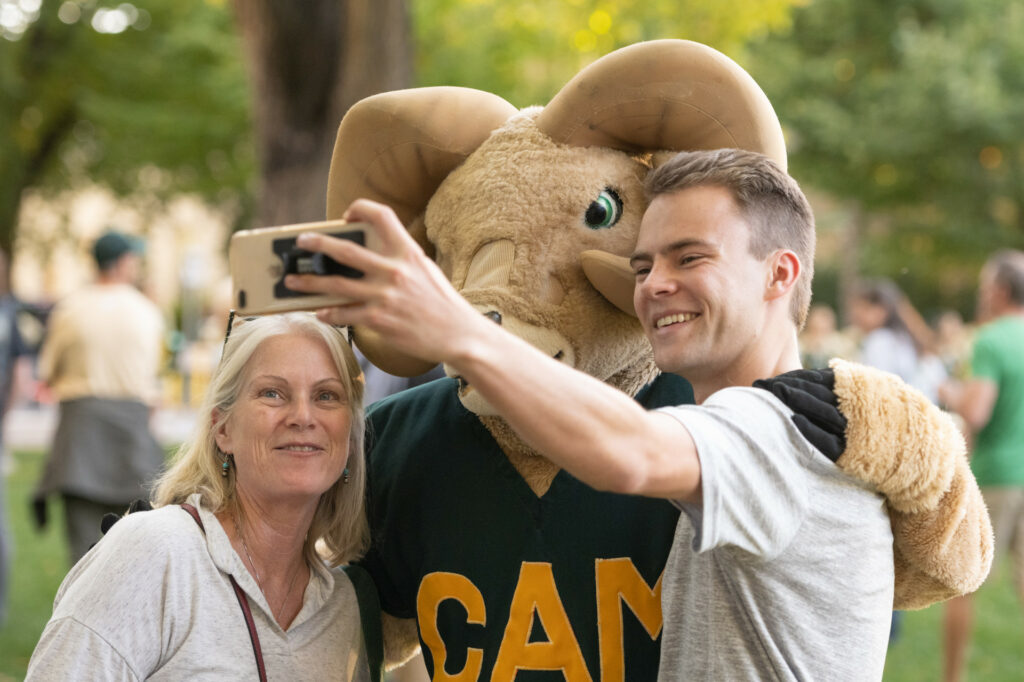A student taking a selfie with Cam the Ram and a family member